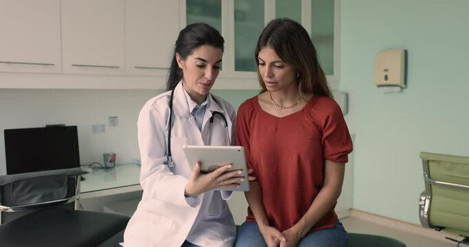 GP and patient using tablet for examining test result, discuss treatment options. Doctor answers client questions about medication information, review diagnostic images, exploring preventive measures