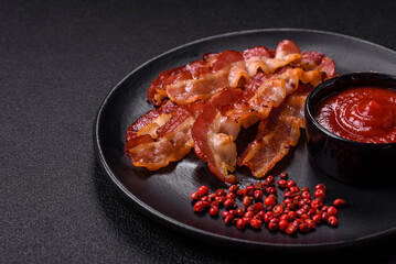 Delicious fresh fried bacon with salt and spices on a dark background