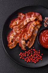 Delicious fresh fried bacon with salt and spices on a dark background