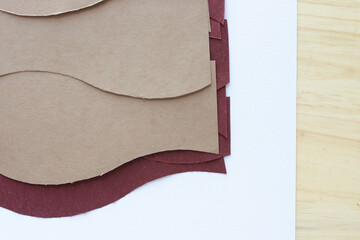 cut brown and red paper with similar wavy edge on blank paper and wood