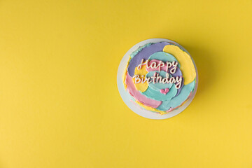 Flat lay of birthday cake with colorful cream cheese smears and happy birthday text on top. Yellow background. Congratulation and invitation to the birthday party