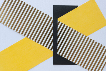 two paper stripes one with gold and white stripes and the other with yellow solids tucked inside a black paper geometric shape with slit