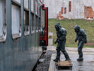 Three men in hazmat suits are standing on a platform next to a train