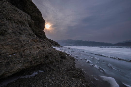 icy mountain lake with rocks, snow and hummocks in early spring in gloomy weather, Bartogay reservoir in Kazakhstan.