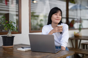 Young woman enjoying the atmosphere and coffee in an outdoor cafe area, while taking a break from working on the laptop