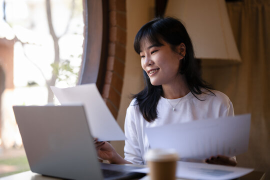 Young Asian woman enjoy with a coffee break while checking, reading documents in hand in a cafe.