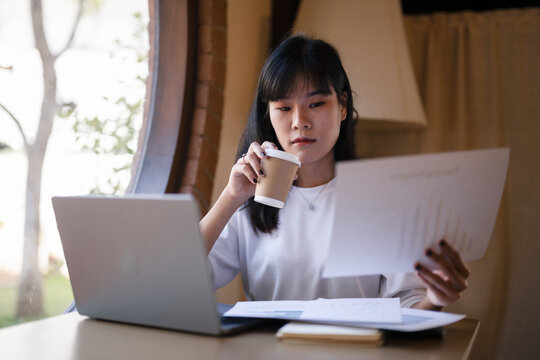 Young Asian woman enjoy with a coffee break while checking, reading documents in hand in a cafe.