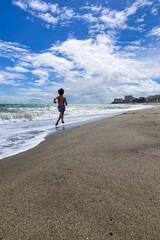 Child running on sand along waves