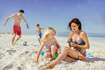 Family fun on the beach with children playing and mother applying sunscreen