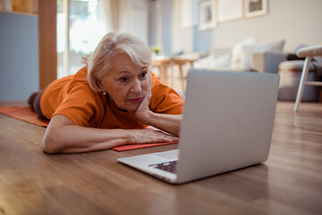 Senior woman using a laptop while doing yoga at home