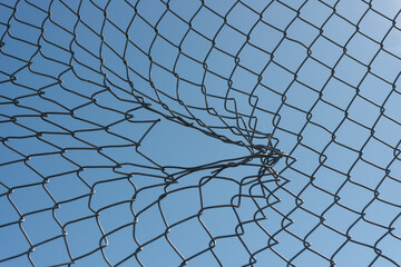 tear in a chain link fence on a blue sky