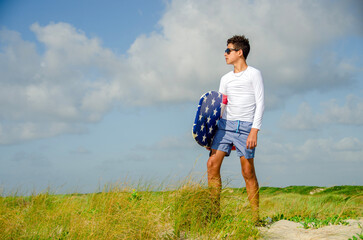 Teenage beach boy carrying his boogie board through tall sea grass