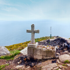 Cross and fireplace (where in  tradition travelers burned some of their clothes at the end of the way, and leave wishes) on cape Fisterra,  (Galicia, Spain). Summer foggy weather.