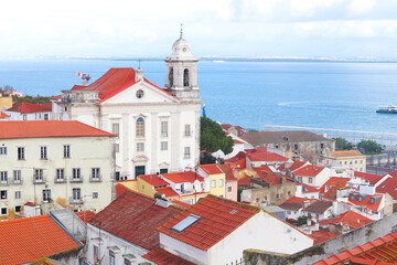 Fototapeta premium View of historical houses with red roofs, Lisbon, Portugal. Amalfa district. The Miradouro de Santa Luzia viewpoint. The Church of Sao Vicente of Fora in the background.