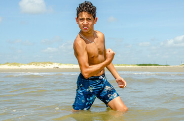 Shirtless male teenager in the water at the beach flexing his muscles