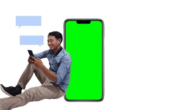 Animation Full size asian young man in blue shirt sitting near big blank screen mobile phone with mockup area using smart phone isolated on plain white background