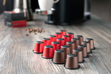 Many multi-colored capsules for a coffee machine lie on a beautiful wooden table against the background of the kitchen.