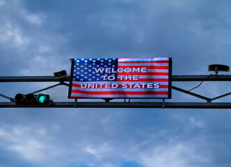 Digital Sign with American Flag stating Welcome To The United States against a cloudy sky.The image was taken at the Otay Mesa Border crossing betwen the USA and Mexico