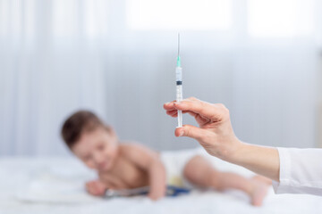 a doctor's hand with a syringe on the background of a small child, a pediatrician gives an injection to an infant