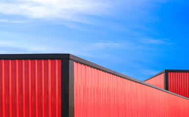 Red and black aluminium roofs of two metal industrial warehouse buildings against blue sky...