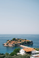 Fototapeta na wymiar View over the red roofs of old houses to the island of Sveti Stefan. Montenegro