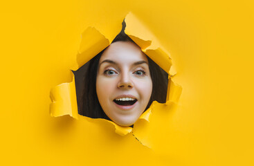 A laughing dildo girl looks out from a torn hole in yellow paper and smiles cheerfully. The concept...