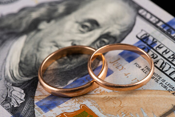 Gold wedding rings against the background of a fragment of a 100 US dollar bill