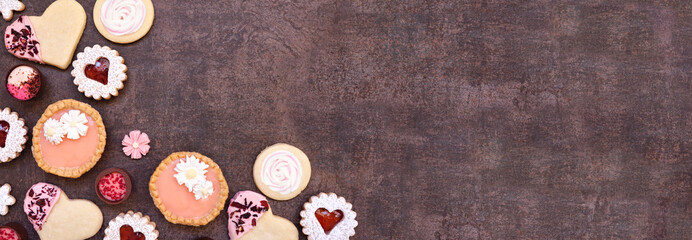 Obraz premium Mothers Day or love themed baking corner border with assorted cookies and sweet treats. Above view on a dark stone banner background with copy space.