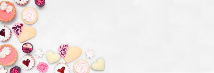 Mothers Day or love themed baking corner border with a variety of cookies and sweet treats. Overhead view on a white marble banner background with copy space.