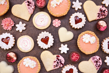 Mothers Day or love themed baking background with an assortment of cookies and sweet treats. Overhead view on a dark stone background with copy space.