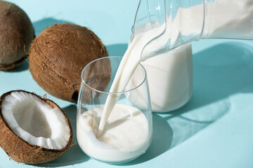 Coconut milk pouring into a glass among coconuts on a blue background..