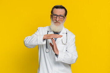 Tired serious upset senior elderly doctor cardiologist man showing time out gesture, limit or stop...