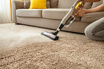 Unrecognizable Person Using a Cordless Handheld Vacuum wash Cleaner on a Beige Carpet at Home