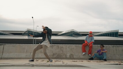 Handsome break dancer enjoy perform freestyle movement with asian friend cheering behind. Hipster...