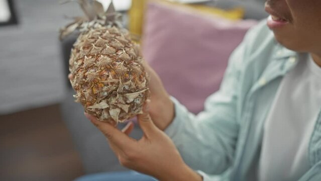 Asian man examines pineapple in a cozy interior setting, displaying curiosity and lifestyle