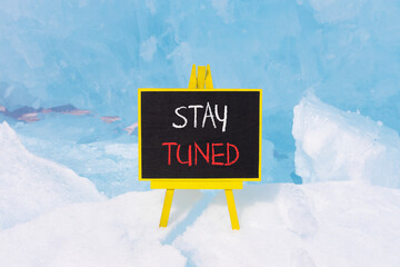 Stay tuned symbol. Concept words Stay tuned on beautiful yellow black blackboard. Beautiful blue ice background. Business, support, motivation, psychological and stay tuned concept. Copy space.
