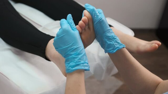 Skilled female masseur in rubber gloves giving foot massage to young woman at beauty salon.