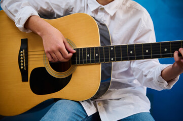 Child's hand plucking the strings while playing the guitar. Cropped view of a teen boy learning to...