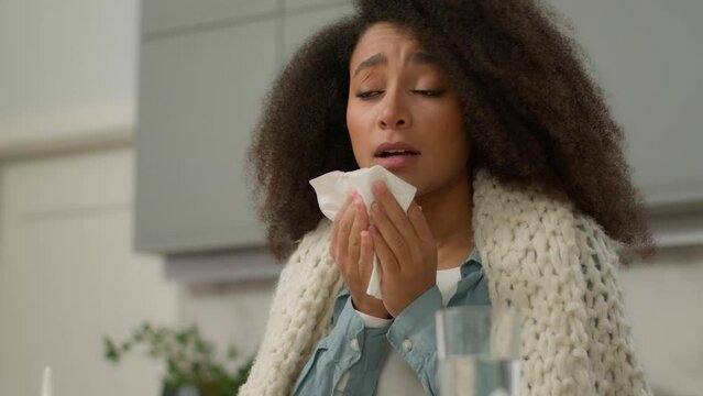 Sick ill African American woman girl female bad feeling unhealthy health problem symptom allergy sneeze suffer rainy nose blow in napkin sneezing cold virus rhinitis disease at home kitchen medicine