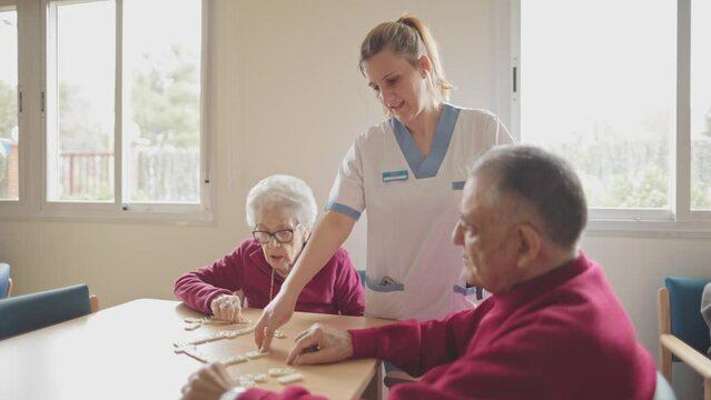 Nurse with seniors playing dominoes at care home