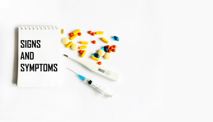 Fototapeta na wymiar On a white background, a thermometer, pills and a notepad with the text SIGNS AND SYMPTOMS. Medical concept