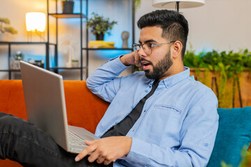 Close-up of surprised Indian man using laptop, receive good news shocked by sudden victory...