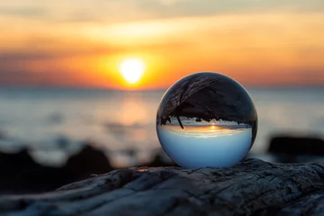 Fotobehang Glass ball  lies on  wood in which the beach and the sea are reflected © Claudia Evans 