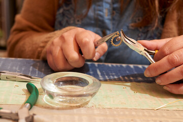 A close-up image capturing the intricate process of a jewelry maker at work. The hands are focused,...