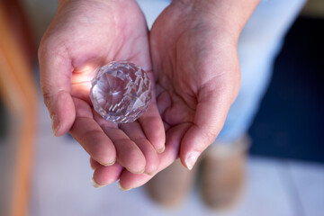 A pair of hands gently holds a clear, intricately cut crystal, illuminating its complex patterns...