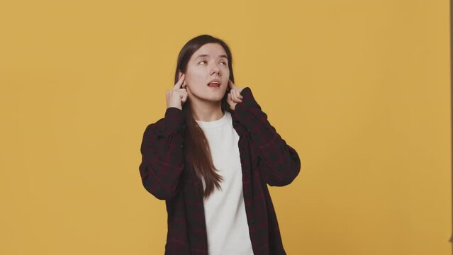 Young woman doesn't want to hear about anything and plugs her ears with her fingers with an absent expression on her face on a yellow background. Concept of lack of interest