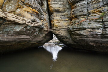 A stream of water passes under a rock formation at a nature park. 