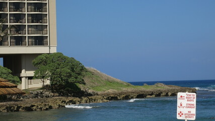Ocean side outcropping with tree and building.  No lifeguard on duty