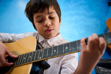 Close-up portrait of confident teenager boy plucking strings while strumming his guitar with...