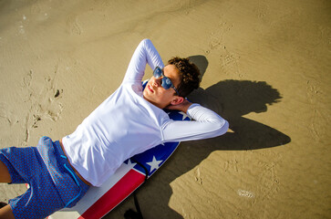 Teenage beach boy with sunglasses lying on his boogie board relaxing with his arms behind his head